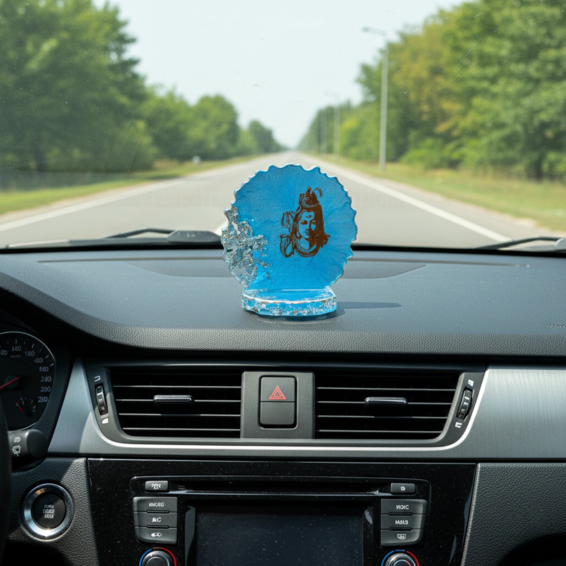 Blue decorative item with a figure on a car dashboard with a road and trees in the background