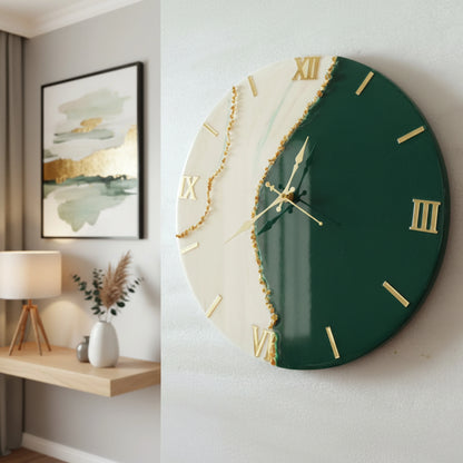Green designer wall clock with gold accents on a white wall, with a shelf and lamp in the background.